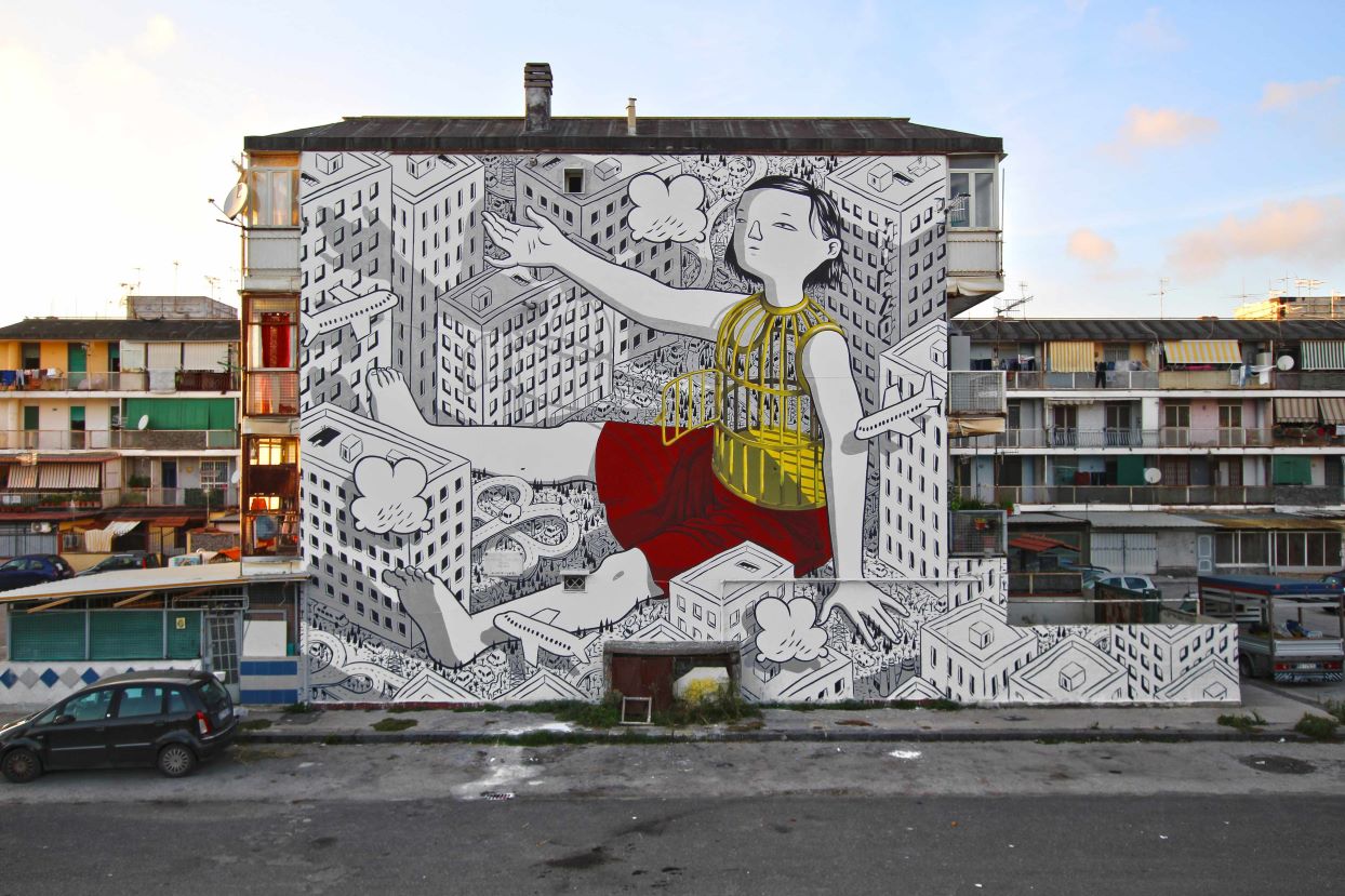 Immagine che contiene un murales su un palazzo che raffigura una ragazzina seduta in mezzo a dei palazzi con la parte superiore del corpo formata una gabbia per uccelli aperta Millo, Open, Murales, Naples, 2019